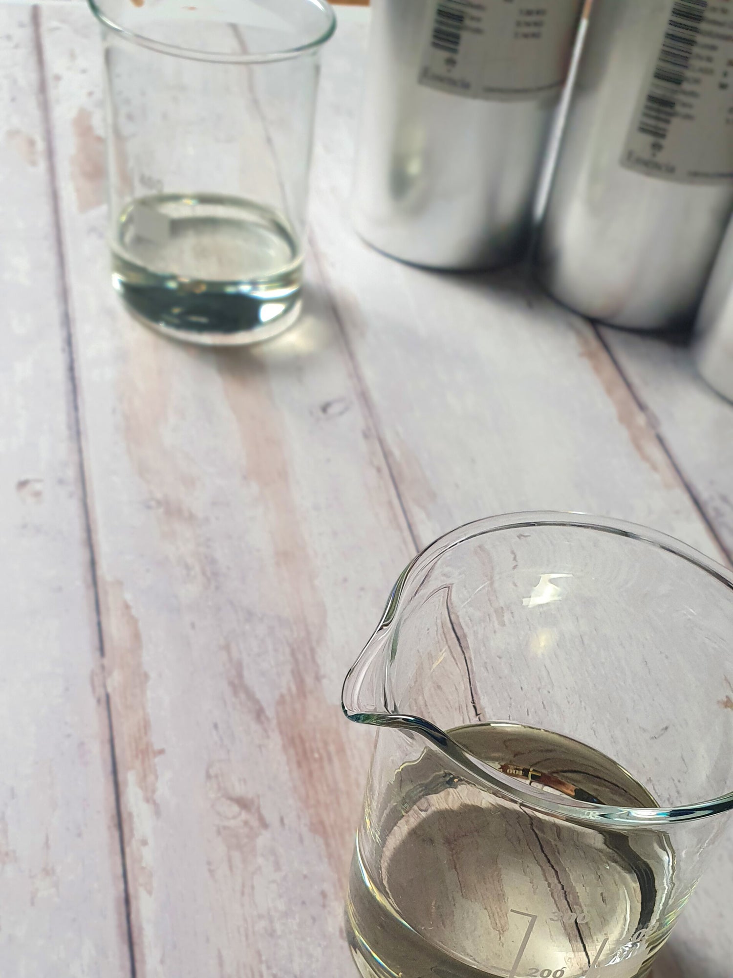 Glasmesskrug mit ätherischen Ölen auf einem weissen Holztisch. Im Hintergrund sind Flaschen mit ätherischen Ölen sichtbar.