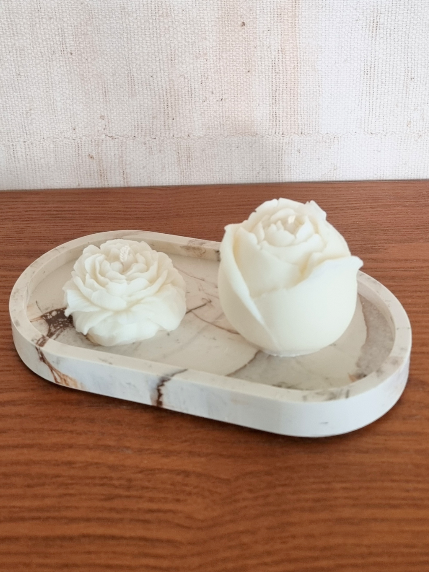 Eine Rosen- und eine Pfingstrosenkerzeauf einem Kerzenteller mit bräunlichem Hintergrund
