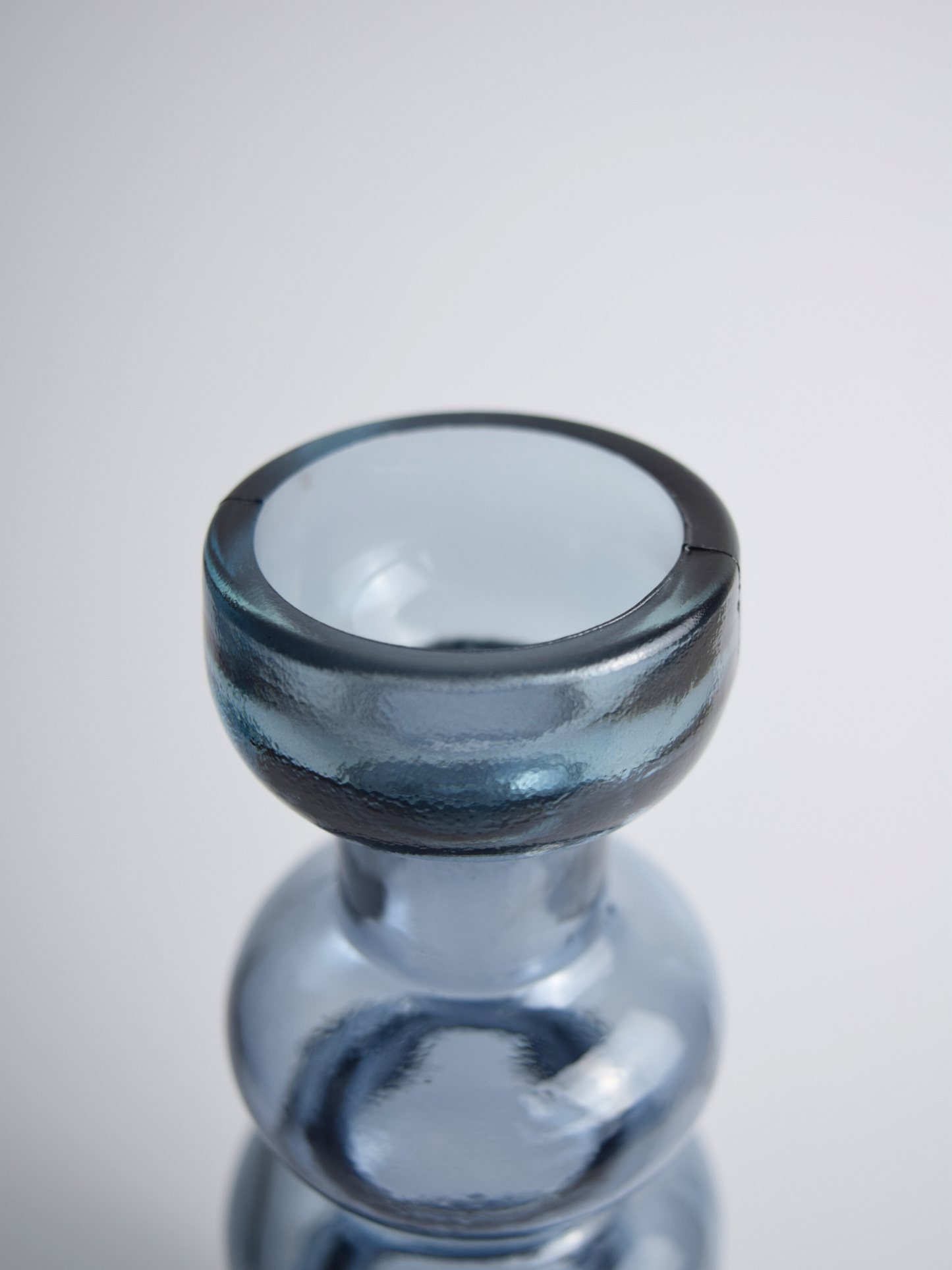 Nahaufnahme eines blauen, gewölbten Kerzenhalter vor einem weissen Hintergrund