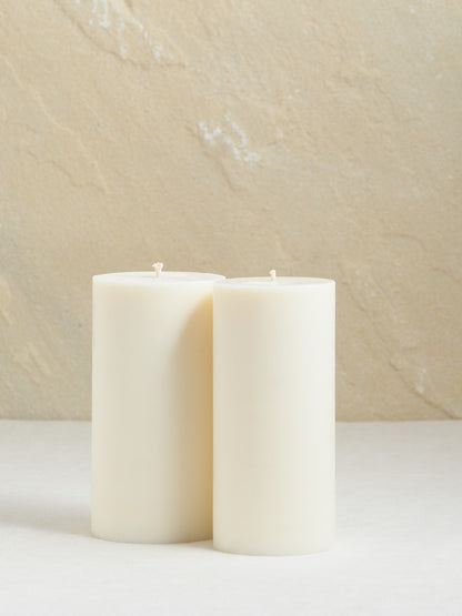 2 grosse glatte, cremeweisse Zylinderkerzen auf beigem Hintergrund.