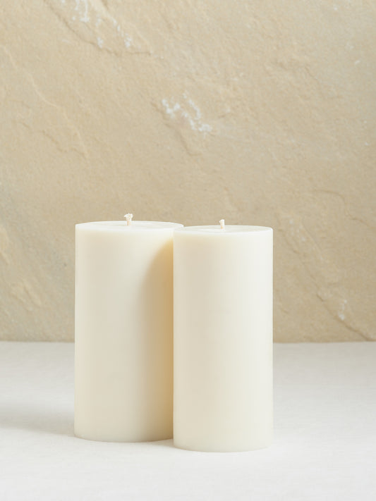 2 grosse glatte, cremeweisse Zylinderkerzen auf beigem Hintergrund.